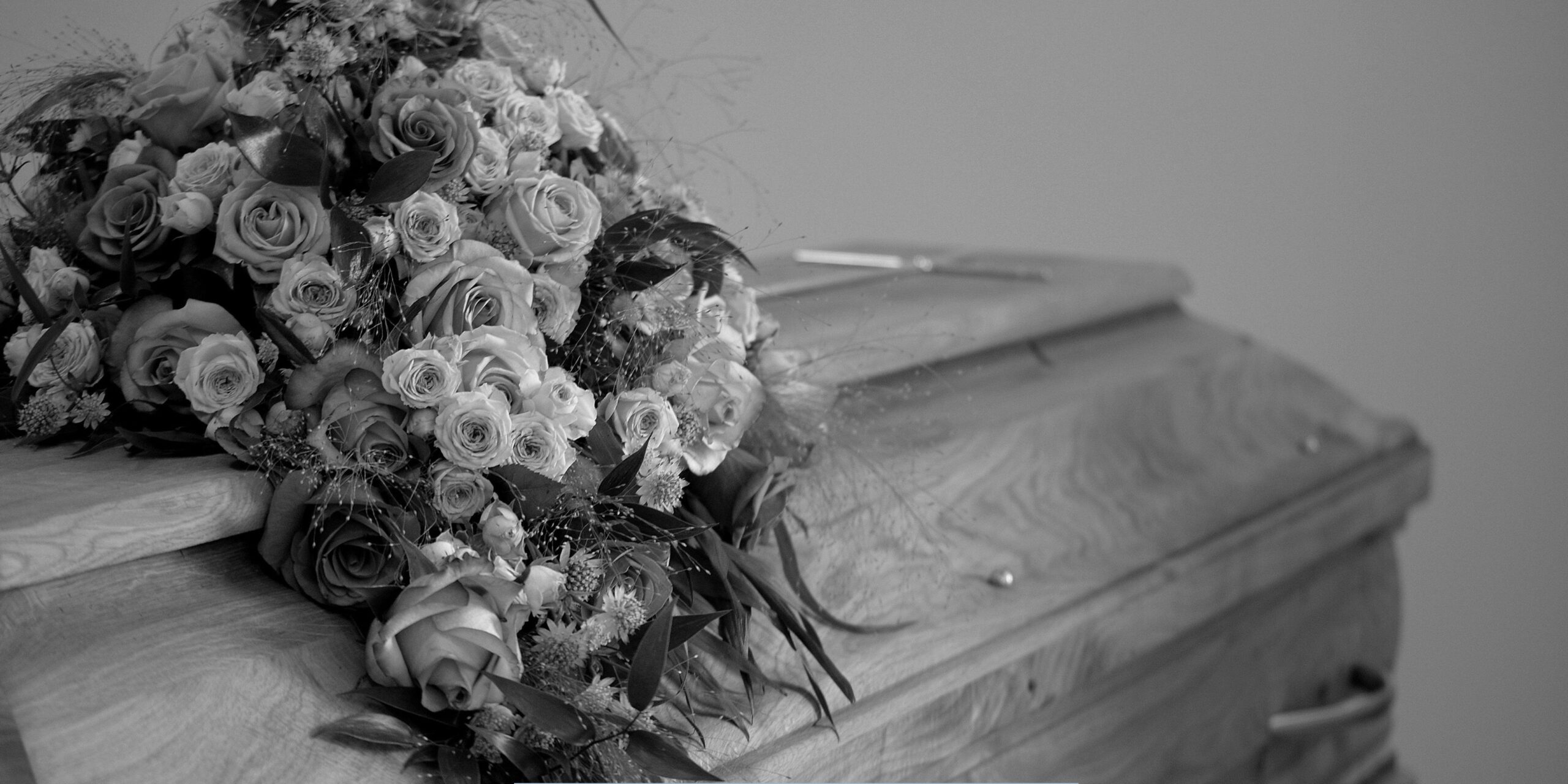 Elegant rose bouquet resting on a wooden casket at a service provided by a funeral home and cremations in Kansas City, MO.