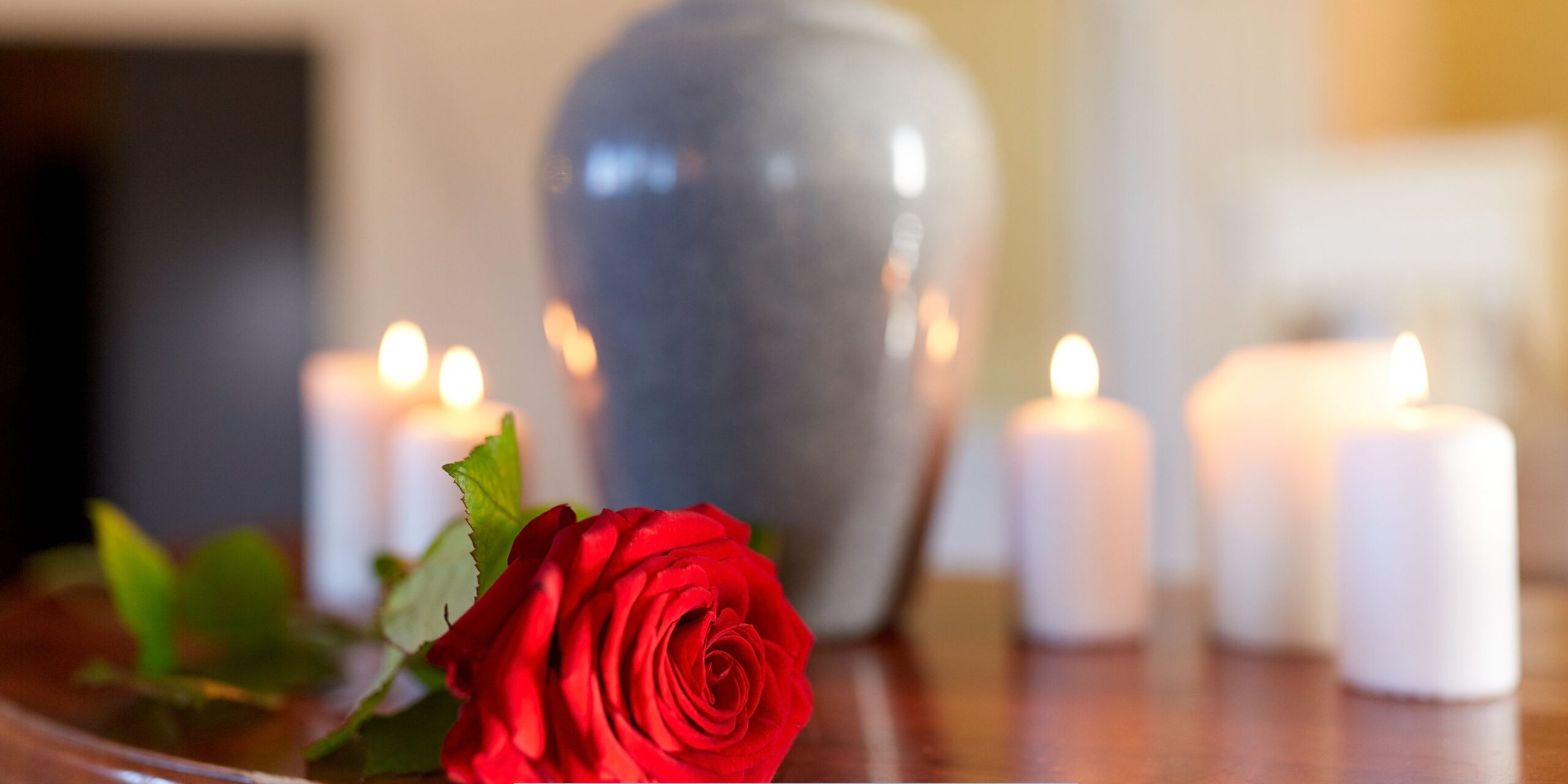 Funeral home and cremation services represented by a memorial urn, red rose, and softly lit candles in a peaceful setting