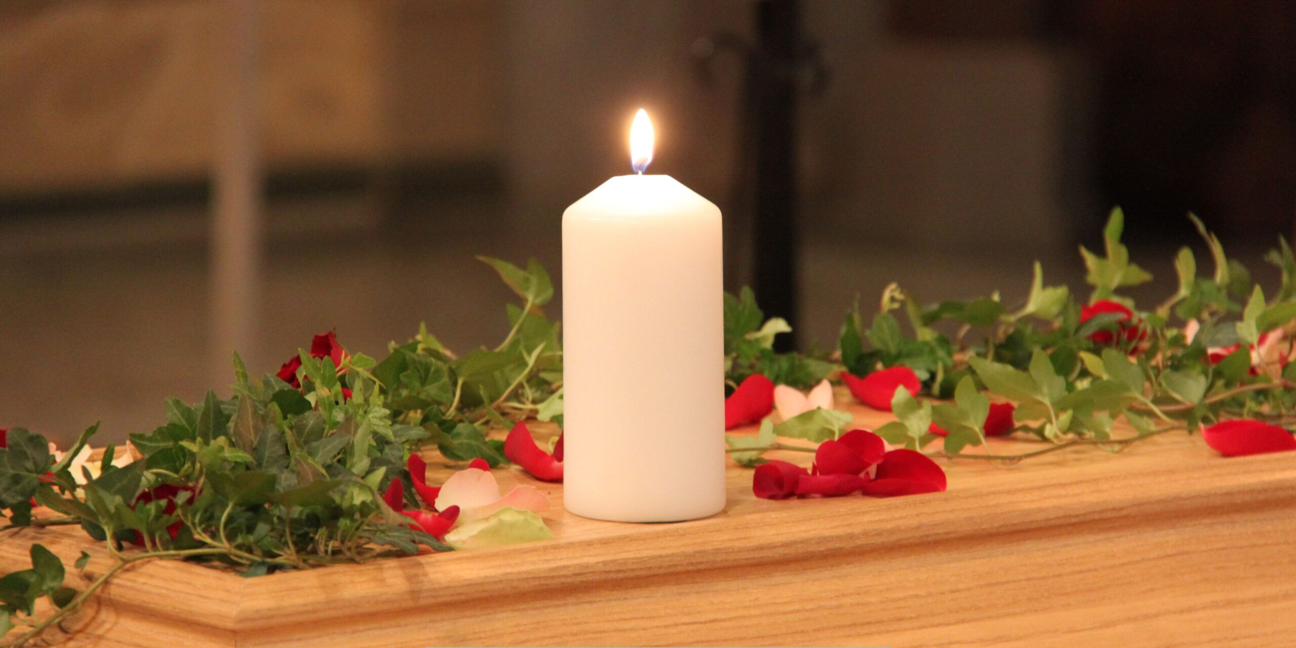 Lit memorial candle with rose petals and greenery during a funeral home and cremation service.